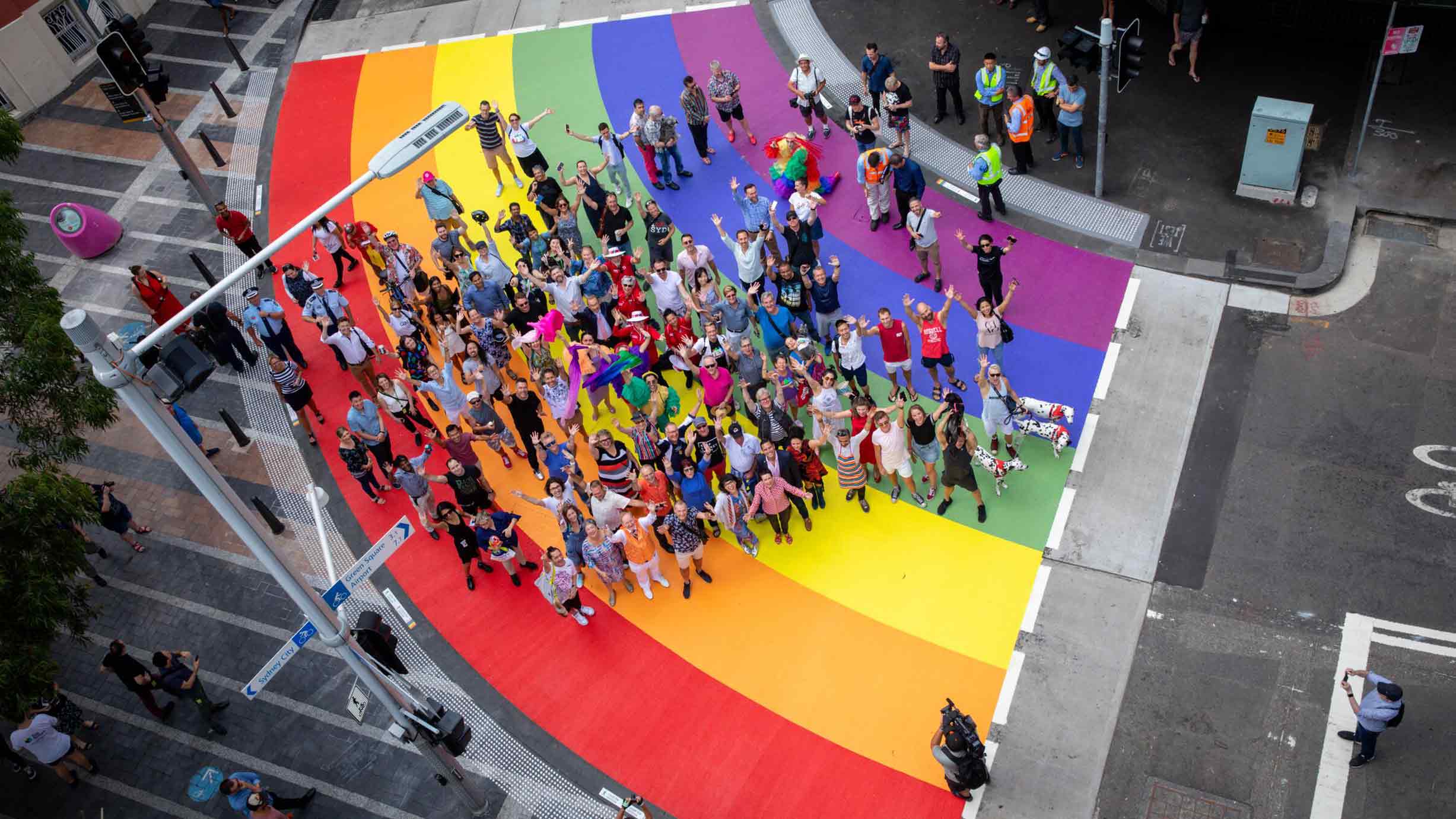 Ariel view of a crown of people standing on a rainbow painted crossing on a city street